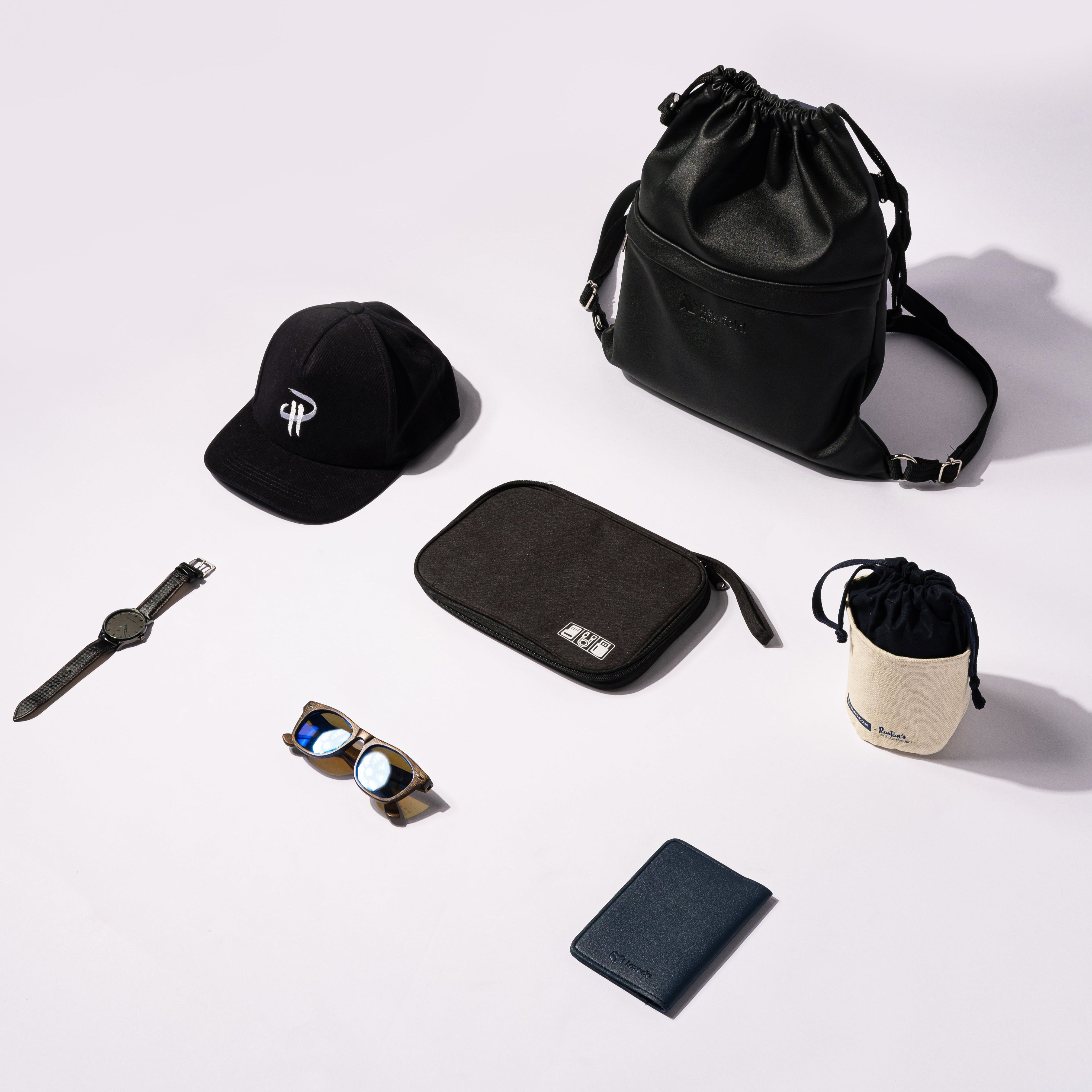 Collection of black travel accessories including a bag, wallet, and hat on a white background