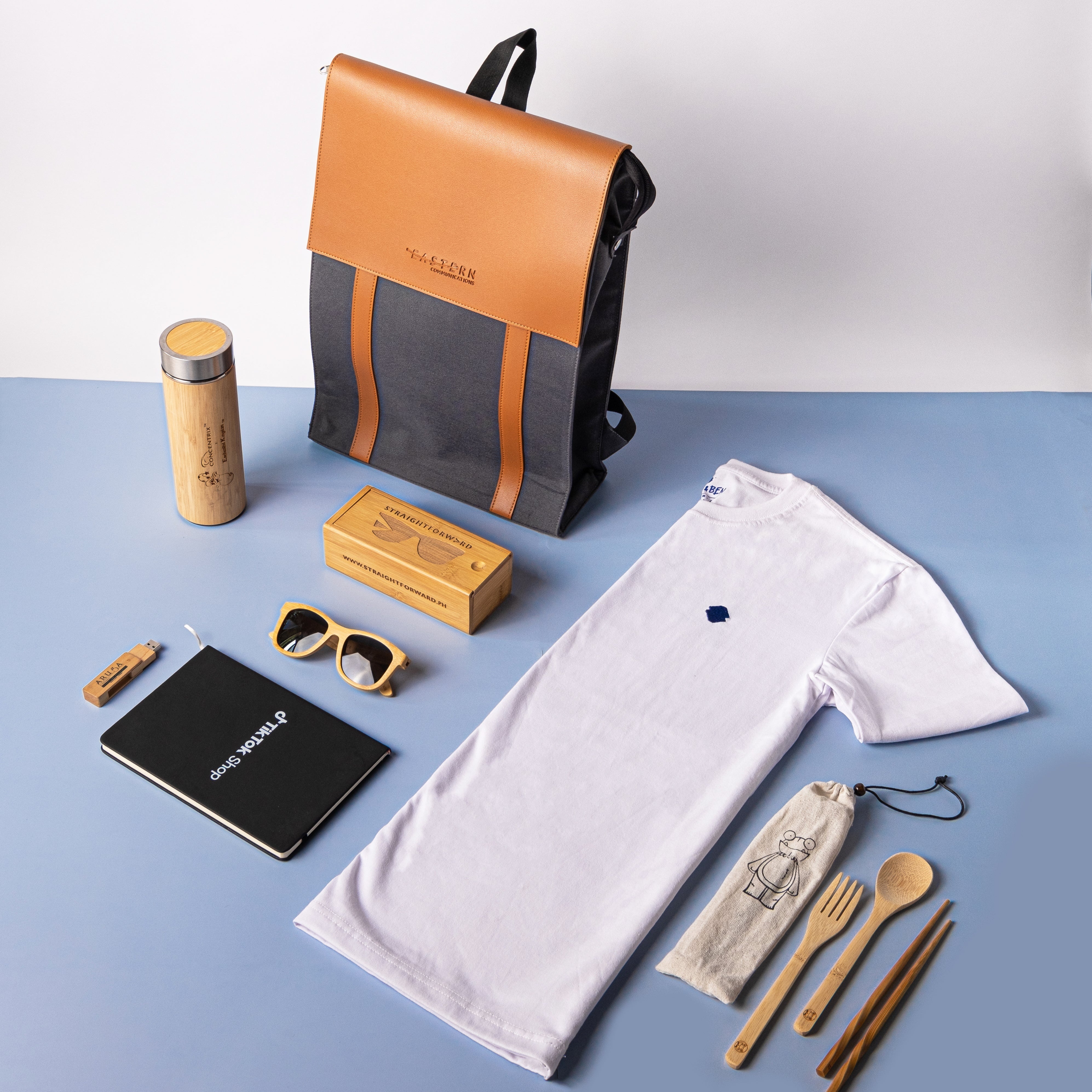 Collection of lifestyle products including a backpack, t-shirt, notebook, and accessories on a blue surface.