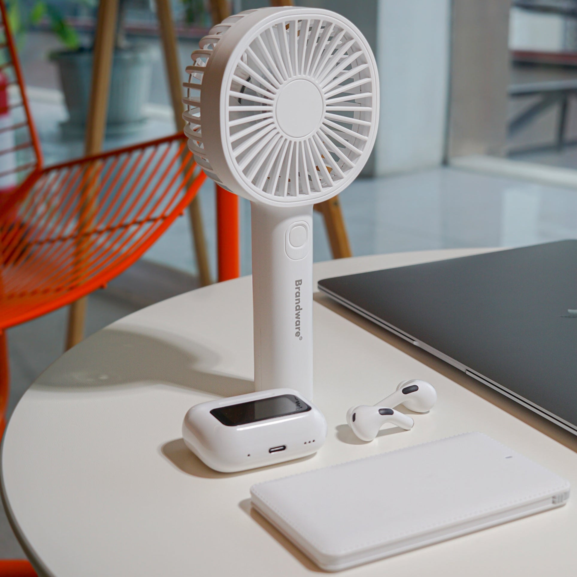 Handheld fan on a table with a laptop and phone in a modern indoor setting